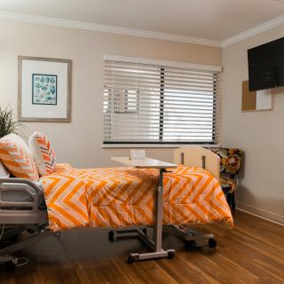 A cozy hospital room with a bed, TV, and window.