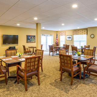 A cozy dining area with wooden tables and chairs, featuring a television and large windows.