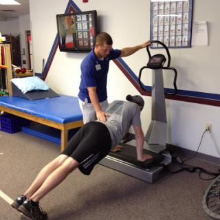 A personal trainer assists a client with push-ups on a vibrating platform.