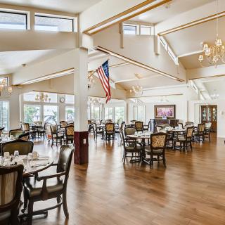 A spacious dining area with elegant chandeliers, set with tables and chairs, featuring a wooden floor and an American flag.
