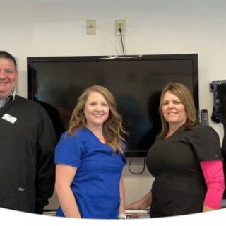 A group of three people smiling indoors in front of a television.