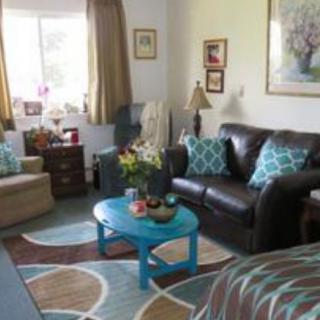 A cozy living room with a sofa, armchair, and a blue coffee table adorned with pillows and decor.