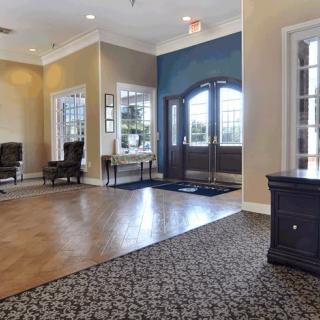 A spacious lobby with a combination of carpet and wood flooring, featuring elegant furniture and large windows.