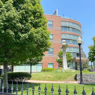 A modern curved brick building surrounded by greenery under a clear blue sky.
