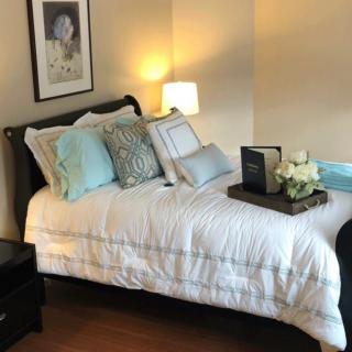 A cozy bedroom with a neatly made bed, decorative pillows, and a bedside lamp.