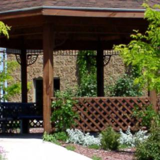 A wooden gazebo with a bench surrounded by plants in a garden setting.