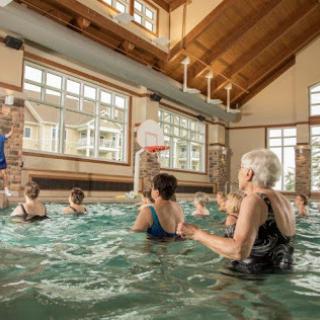 A group of seniors participating in a water aerobics class at an indoor pool, enjoying exercise and social interaction.