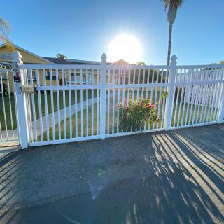 A sunny view of a white fence and gate casting long shadows on the sidewalk.