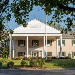 A colonial-style building with a grand entrance surrounded by trees and landscaped gardens.