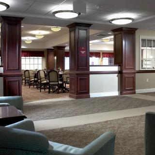 A spacious lobby interior with comfortable seating, decorative columns, and a view of the adjacent dining area.