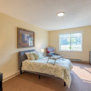 A cozy bedroom with a neatly made bed, a large window, and simple decor.