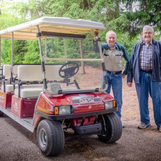 Two people standing next to a red golf cart outdoors.