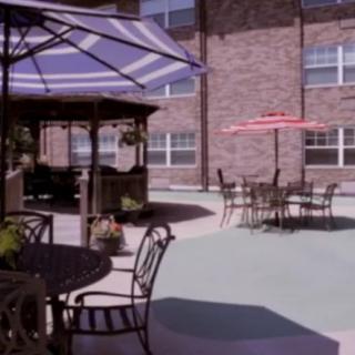 A cozy patio area with tables, chairs, and umbrellas adjacent to a brick building.