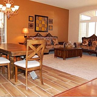 A cozy living and dining area with warm orange walls and wooden flooring, featuring a chandelier, comfortable sofas, and a dining table.