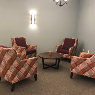 A cozy seating area with patterned armchairs arranged around a wooden coffee table in a softly lit room.