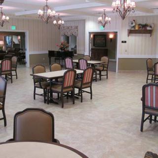 An empty dining room with neatly arranged tables and chairs, adorned with chandeliers.