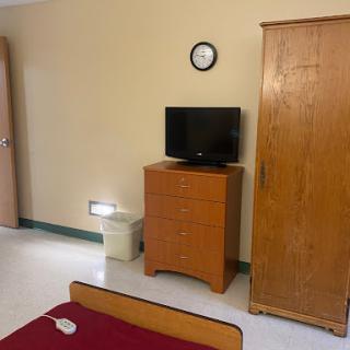 A simple room featuring a bed, a television on a dresser, and a wardrobe.