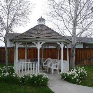 A serene gazebo nestled in a garden, surrounded by blooming flowers and tall trees.
