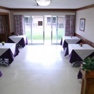 An empty dining room with tables and chairs arranged in a neat order, illuminated by daylight coming through large windows.