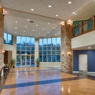 A modern and spacious lobby with wood flooring, stone columns, and ample lighting.