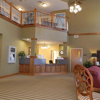 A spacious and well-decorated lobby featuring a reception area with carpeted flooring, chandeliers, and a wooden railing.