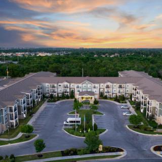 Aerial view of an apartment complex with surrounding greenery and a picturesque sunset.
