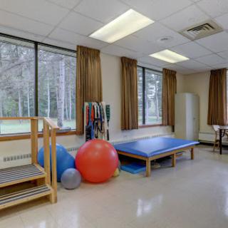 A well-equipped therapy room featuring exercise balls, a treatment table, and wooden steps, illuminated by natural light from large windows.