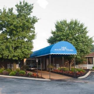 A building entrance with a blue awning and surrounding landscaping.