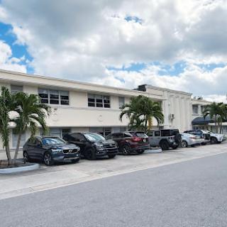 A row of parked vehicles along a building, framed by palm trees under a partly cloudy sky.