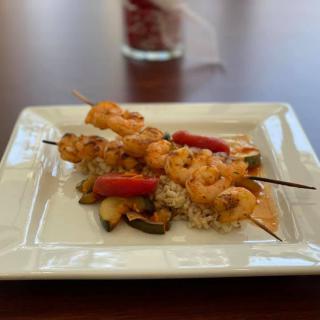 A dish of shrimp skewers with vegetables served on a bed of rice.