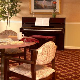 A cozy living room interior featuring a piano with a music sheet, surrounded by a table and chairs.