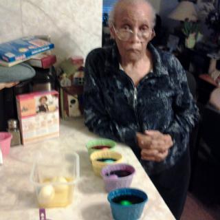 An elderly woman stands in the kitchen, preparing to dye Easter eggs.