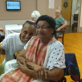 A joyful moment shared between a caregiver and an elderly woman, highlighting the warmth of companionship in a community setting.