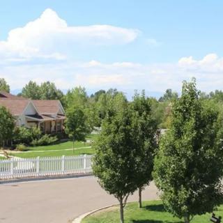 A suburban neighborhood with a house, trees, and a white fence along the street.