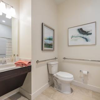 A modern bathroom featuring a toilet, sink with a mirror, wall art, and accessible design elements.