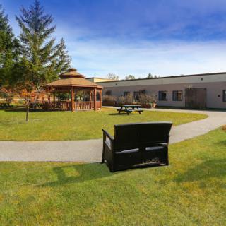 A serene garden with a gazebo, bench, and well-maintained grass under a clear blue sky.