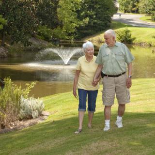 An elderly couple enjoys a leisurely walk by a pond in the park.