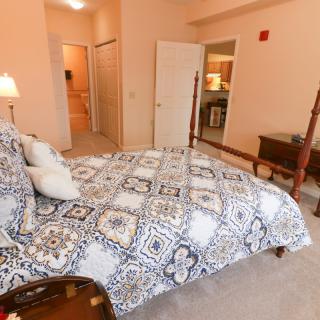 A cozy bedroom featuring a four-poster bed with patterned bedding and a carpeted floor.