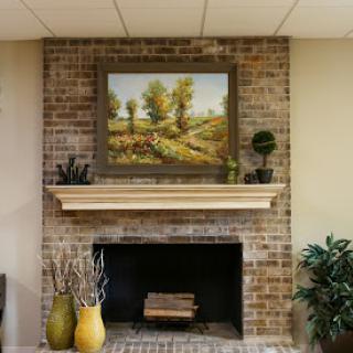 A cozy living room setup featuring a brick fireplace, adorned with a beautiful landscape painting and decorative vases.