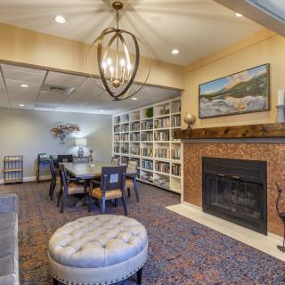 A cozy living room features a warm fireplace, bookshelves filled with books, and a dining table illuminated by an elegant chandelier.