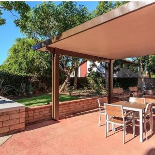 A serene backyard patio with a canopy and outdoor furniture, surrounded by lush greenery.