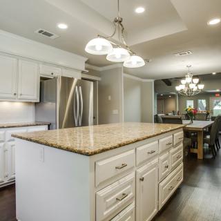 A modern kitchen with a large island and granite countertops, featuring elegant lighting and spacious cabinetry.