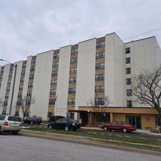 A multi-story apartment building surrounded by parked cars on a cloudy day.