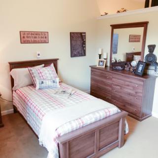 A cozy bedroom featuring a single bed with plaid bedding and a wooden dresser with a mirror.