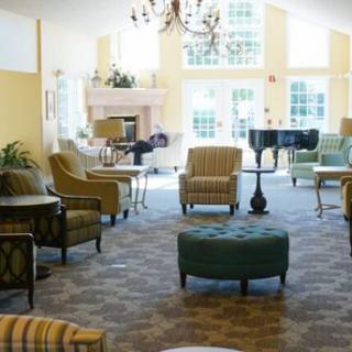 A cozy lounge area featuring comfortable chairs, a grand piano, and large windows offering natural light.
