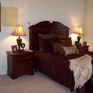 A cozy bedroom with a wooden bed frame, matching nightstands, and elegant lamps providing warm lighting.