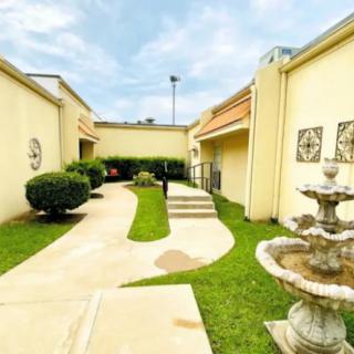 A serene courtyard with a curved walkway, manicured bushes, and a decorative fountain.