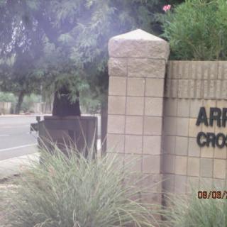 A roadside entrance sign beside a brick wall surrounded by vegetation.