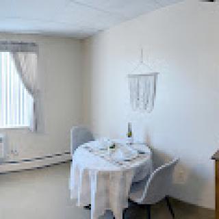 A cozy, minimalist dining area featuring a neatly set table and natural light filtering through the window.