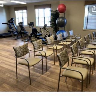 An indoor fitness room with exercise equipment and arranged chairs.